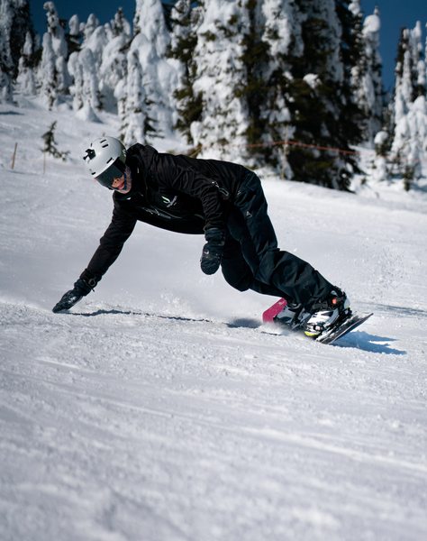 Persona practicando snowboard en una pista nevada entre árboles